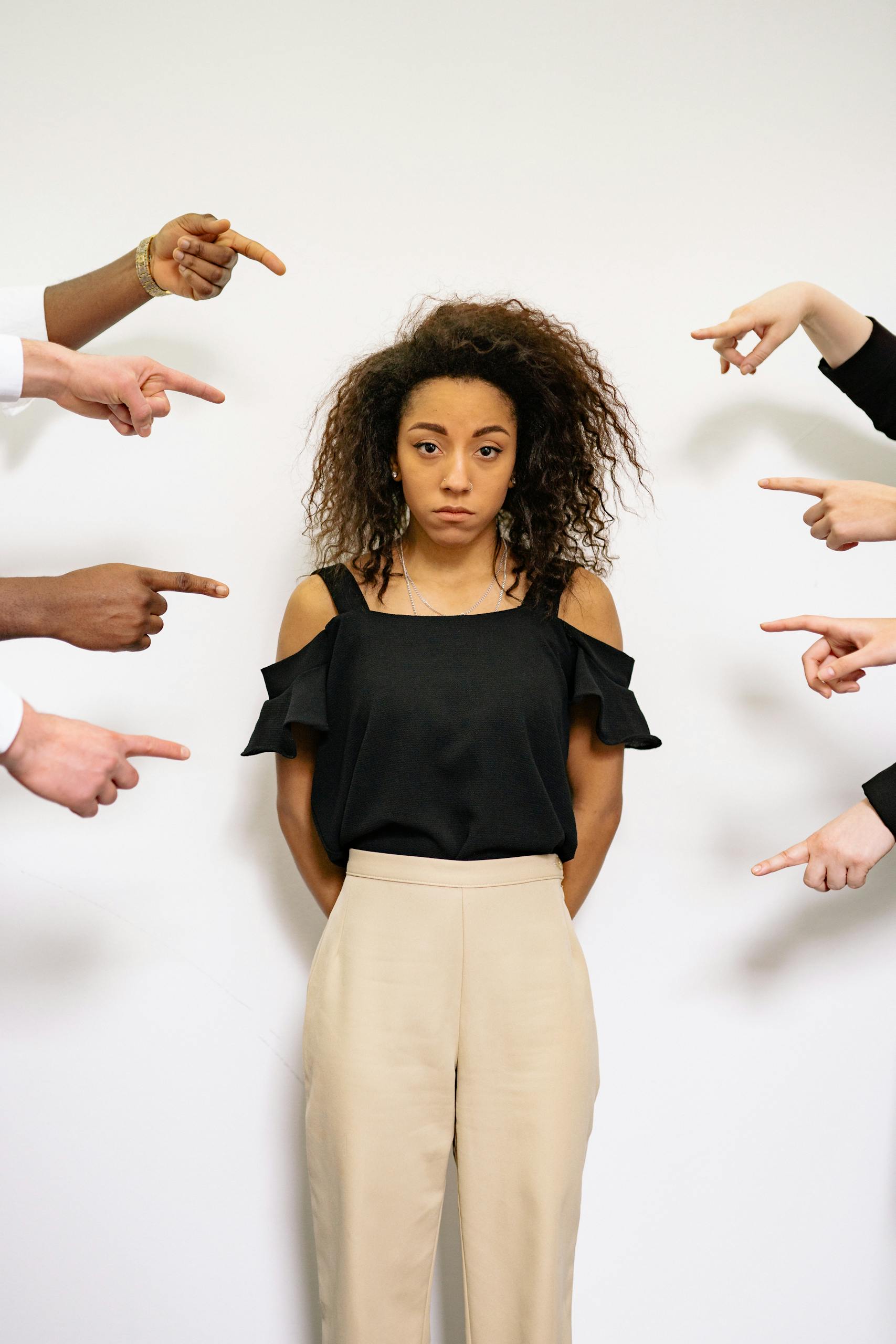 Portrait of a woman surrounded by pointing fingers, conveying themes of accusation and stress.