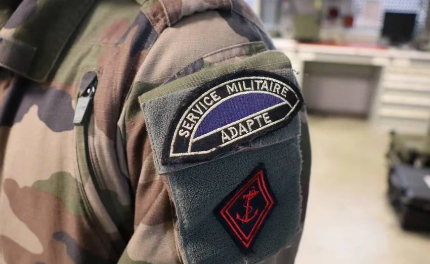 Écusson du Service Militaire Adapté (SMA) sur un uniforme militaire de camouflage avec une ancre rouge dessinée.