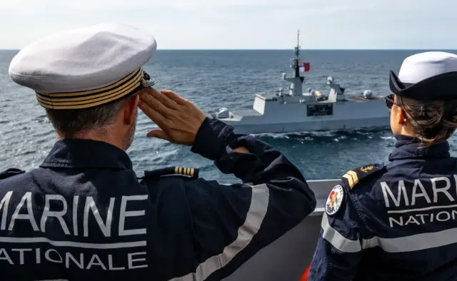 Deux membres de la Marine Nationale, un navire de guerre navigue en arrière-plan en mer