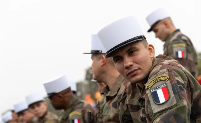 Des soldats de la Légion Étrangère française portent des képi blancs et des uniformes de camouflage. L'un d'eux arbore un écusson 'Légion Étrangère France'