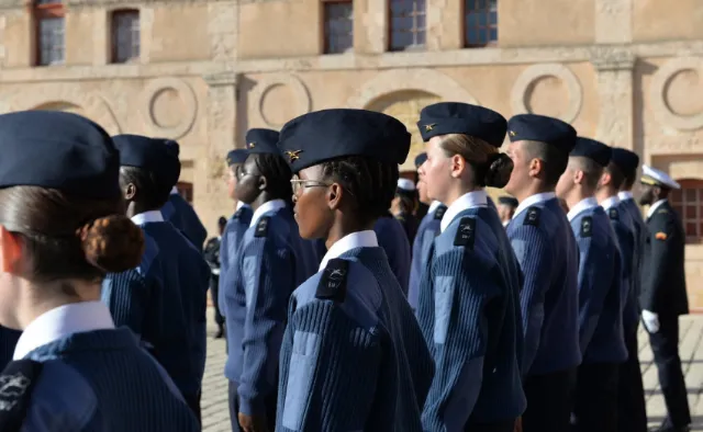 Groupe de cadets en uniforme bleu et casquettes noires, alignés à l'extérieur d'un bâtiment historique.