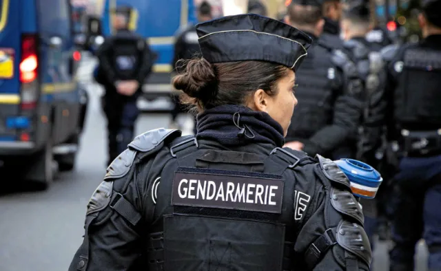 Gendarme portant un gilet tactique avec l'inscription 'GENDARMERIE' dans le dos, en uniforme et casquette.