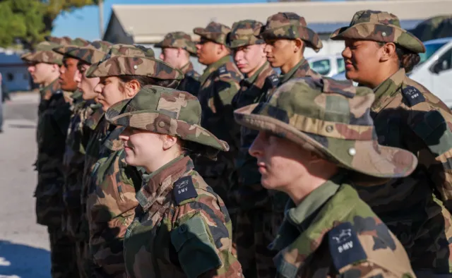 Groupe de militaires en uniforme de camouflage et chapeaux, alignés et regardant dans la même direction.
