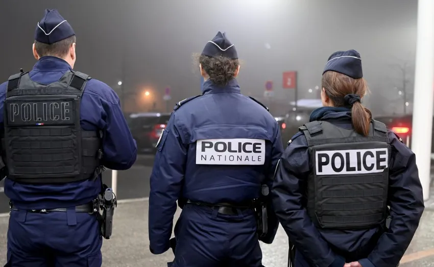 Trois policiers de la Police Nationale se tiennent de dos en uniforme, équipés de gilets tactiques, de nuit.
