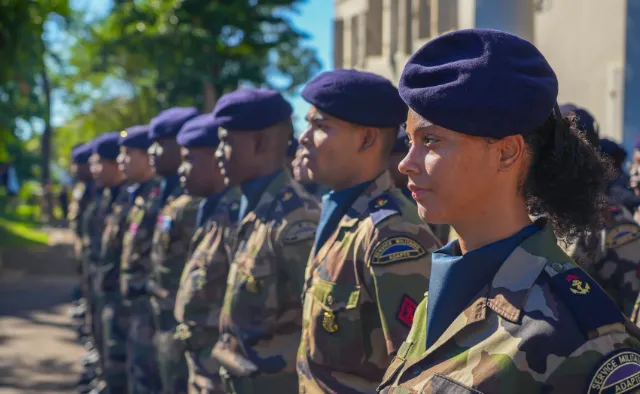 Groupe de militaires en uniforme de camouflage et bérets bleus, alignés et regardant dans la même direction.